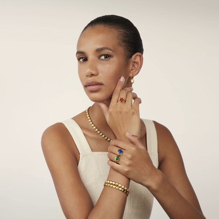 Model wearing gold and gemstone jewellery with tennis bracelet styling in natural summer light