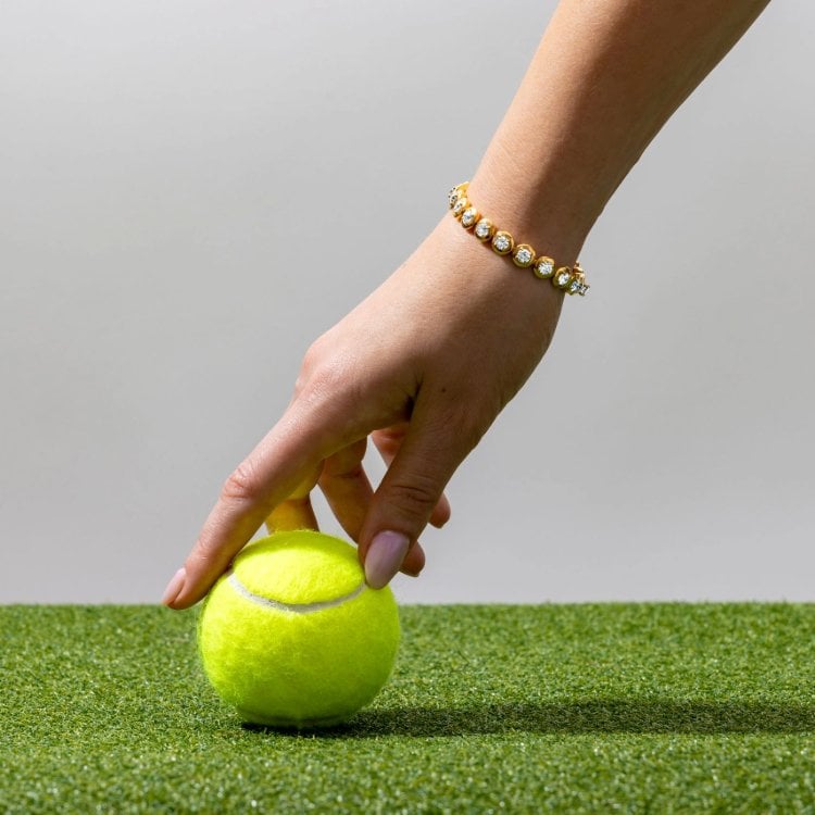 Close-up of diamond tennis bracelet styled on wrist holding a tennis ball